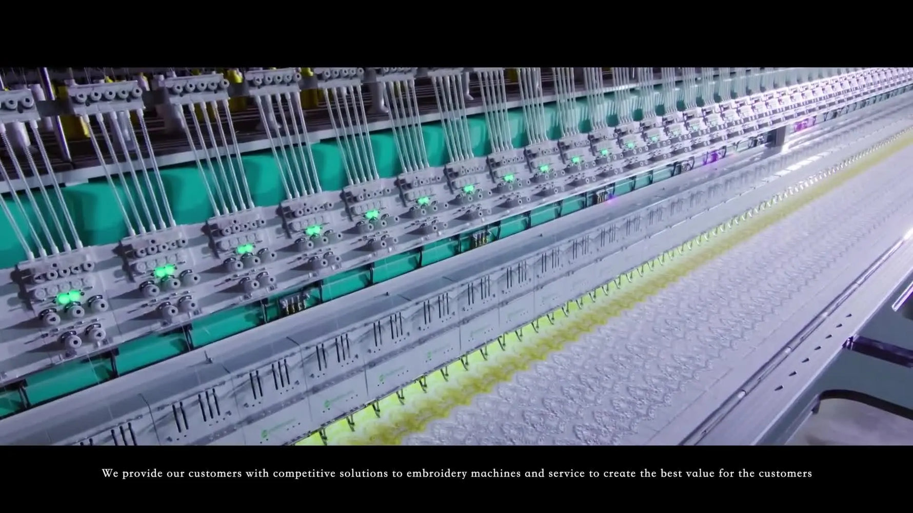 Multiple embroidery heads stitch simultaneously on green fabric, showing the real-world production environment a factory-built multi-head machine is designed for.