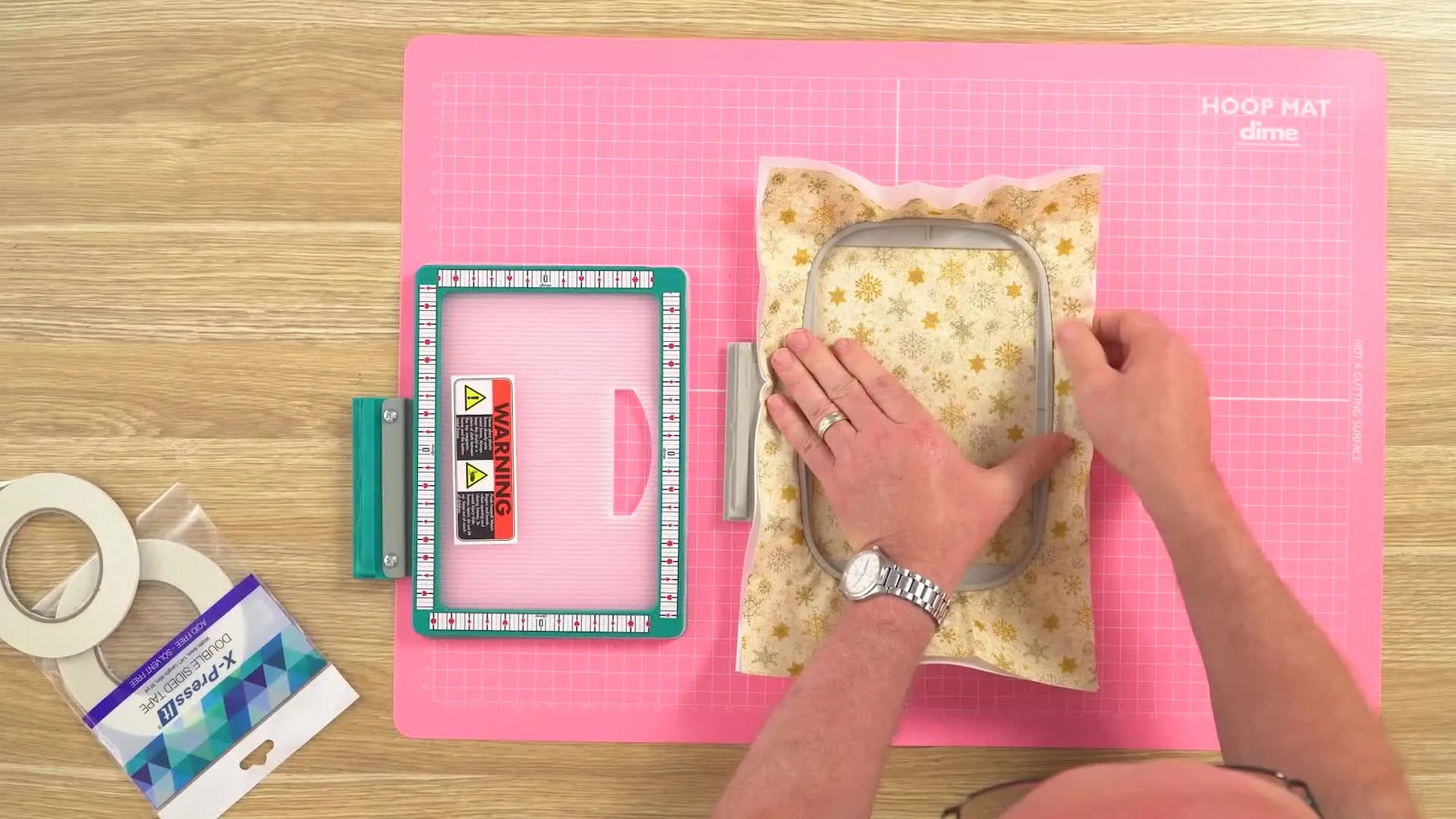 Hands adjust fabric fullness in a hooped piece after applying high-tack tape to improve grip and prevent slippage.