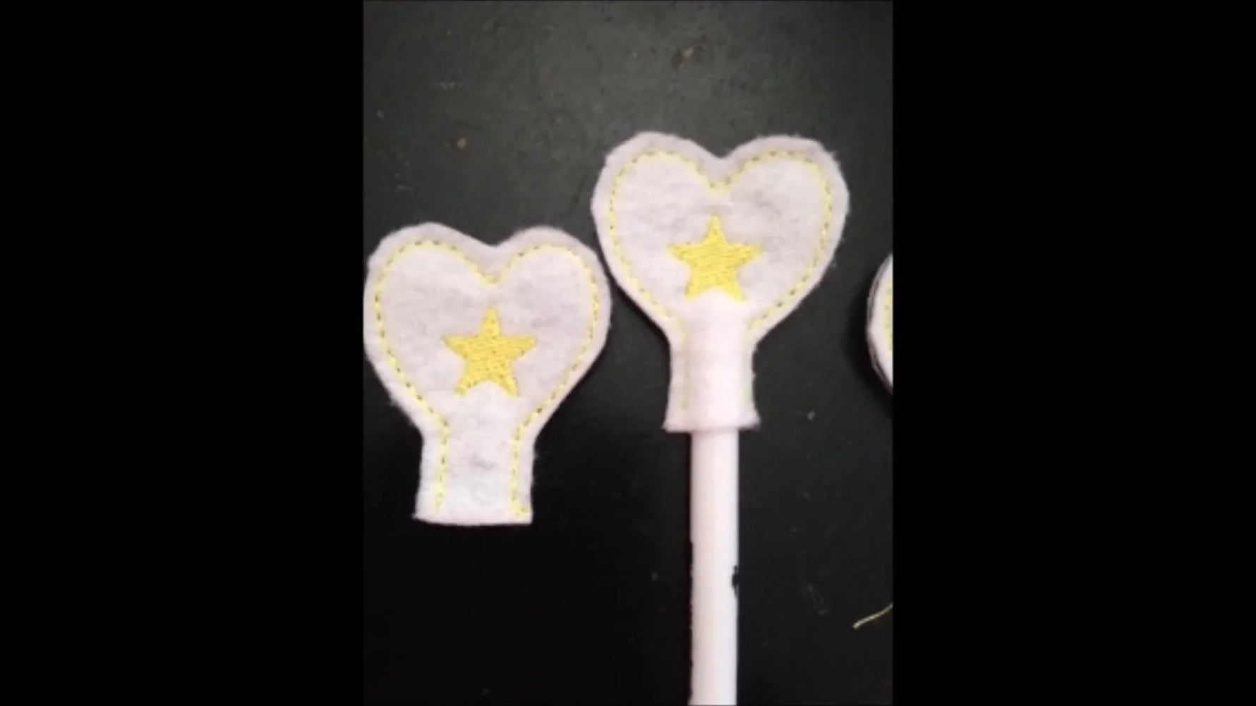 A finished white felt heart pencil topper with a yellow star stitched in the center, shown on a pencil/stick.