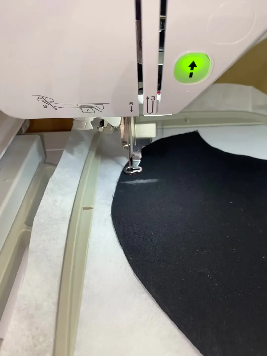 A close-up action view of the embroidery foot stitching pink thread onto black mask fabric, showing how tight edge clearance can get on small cut pieces.