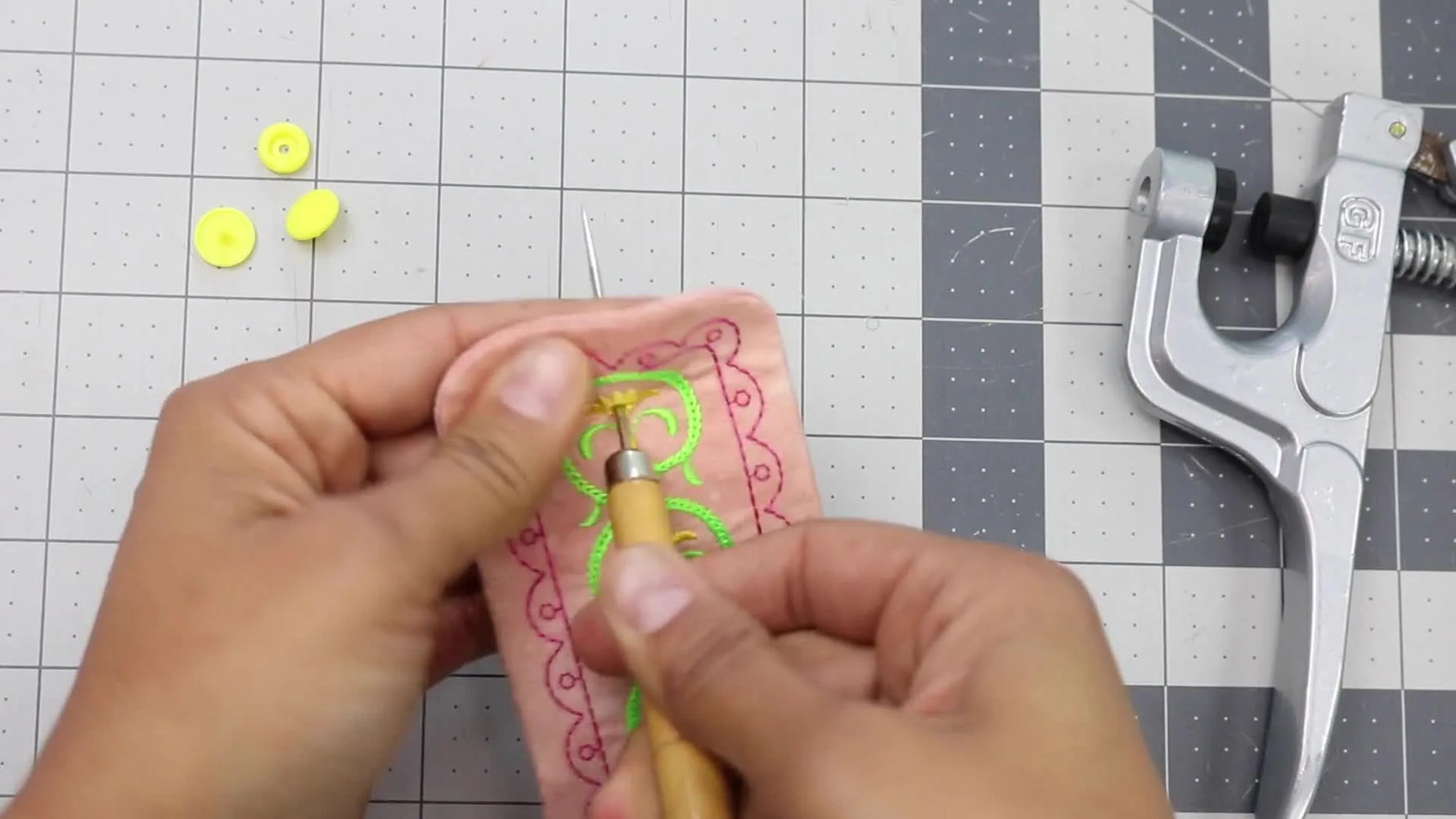 Close-up of an awl piercing the embroidered cord keeper to prep perfectly aligned snap placement.