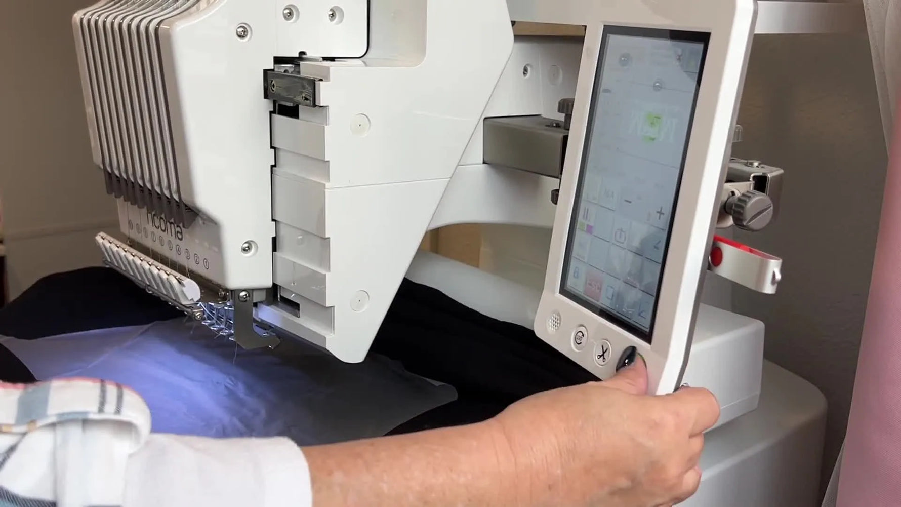 Close-up of the Ricoma EM-1010 stitching a design onto a black hoodie with water-soluble topping under the machine’s blue light.