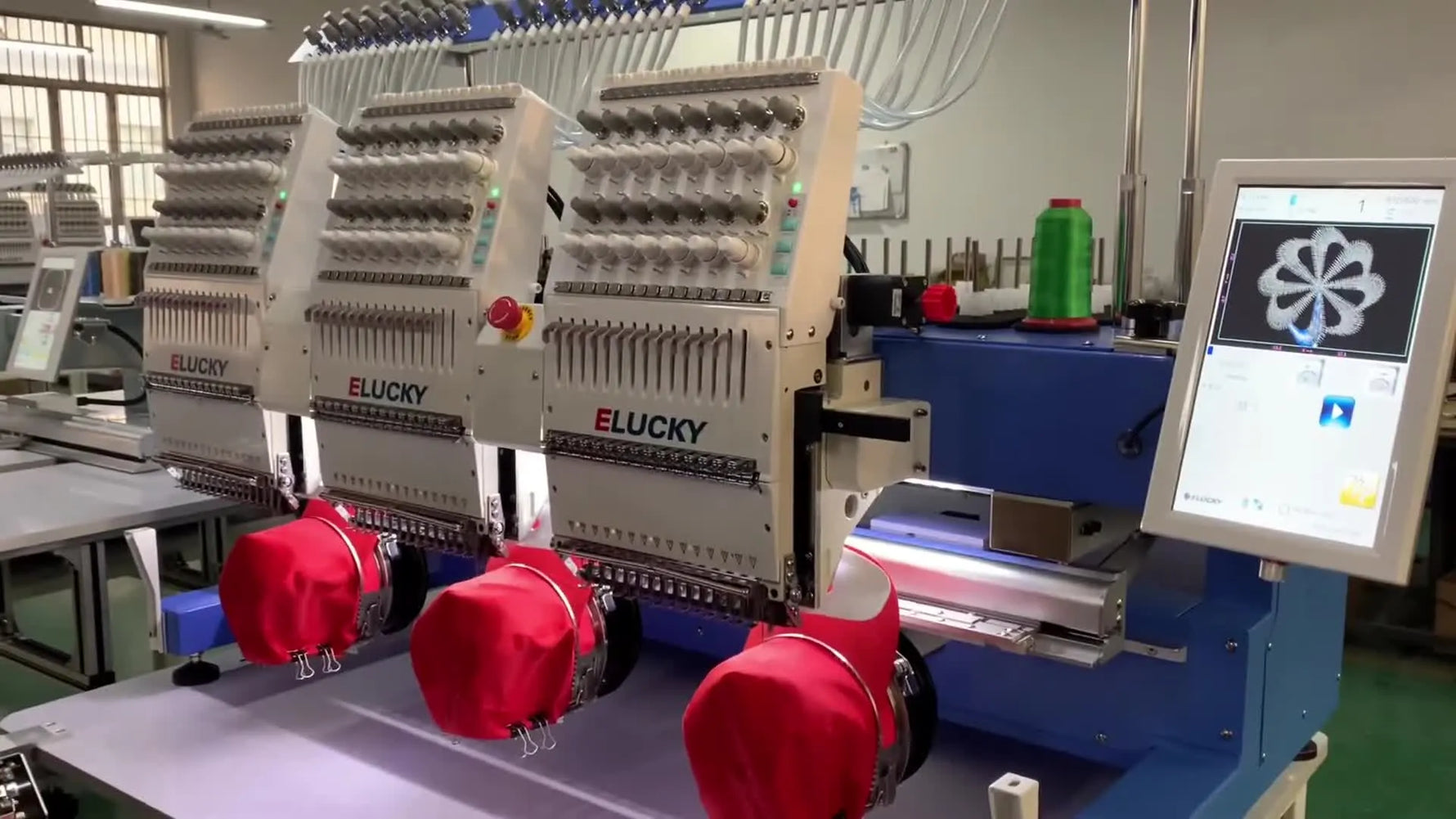 A wide production view of three ELUCKY embroidery heads stitching red caps at the same time, showing a true multi-head workflow in motion.