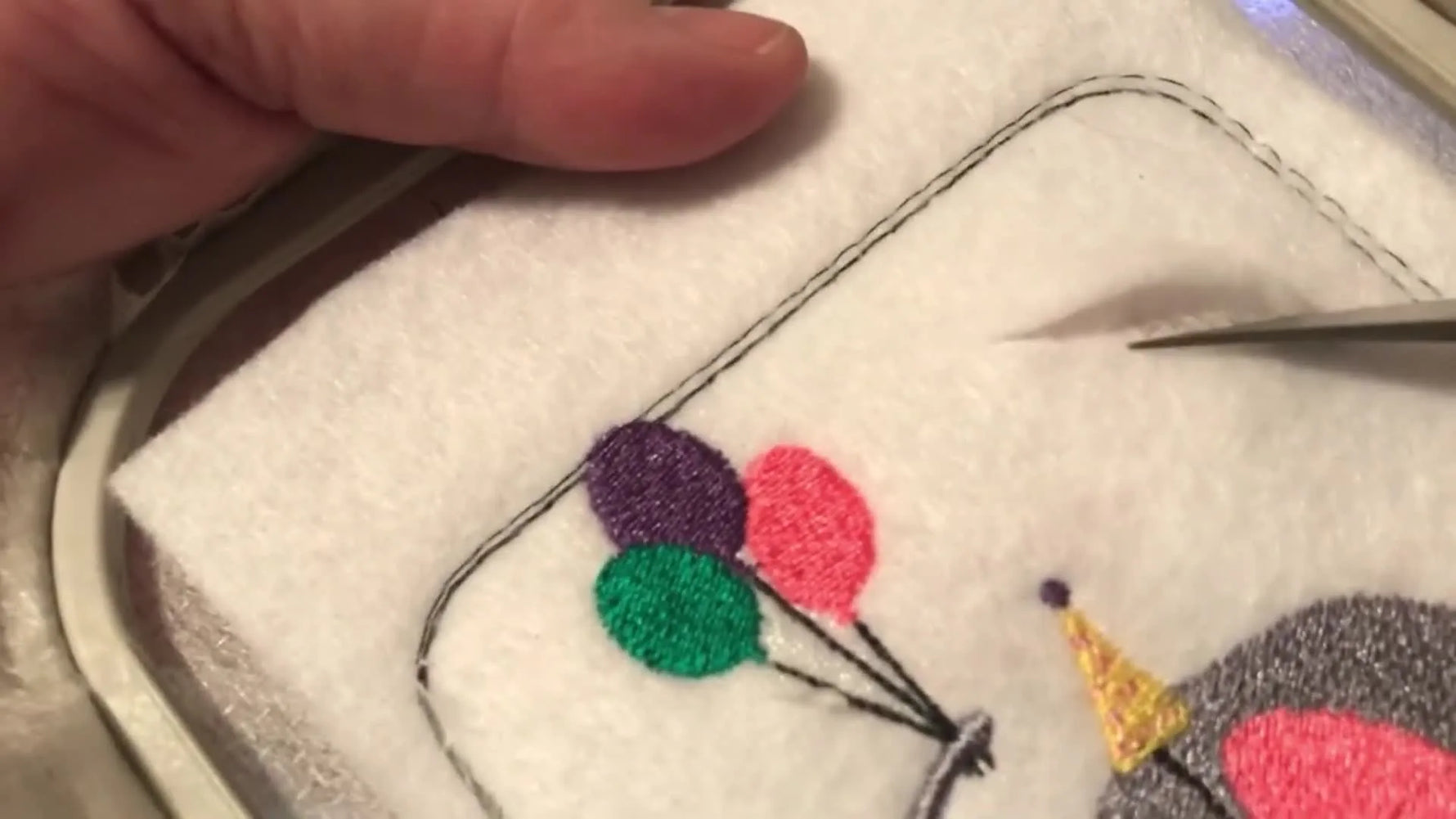 The finished elephant-with-balloons embroidery sits neatly in the hoop, ready to be sealed into a functional felt money pouch.