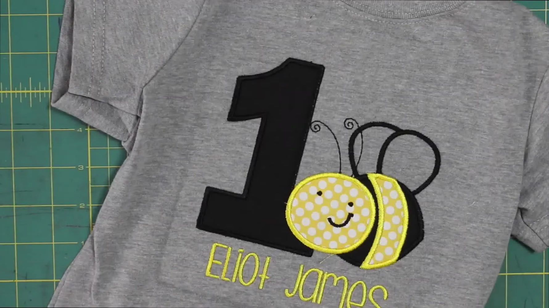 A finished grey birthday T-shirt featuring a bee appliqué and a large number 1, shown flat from above.