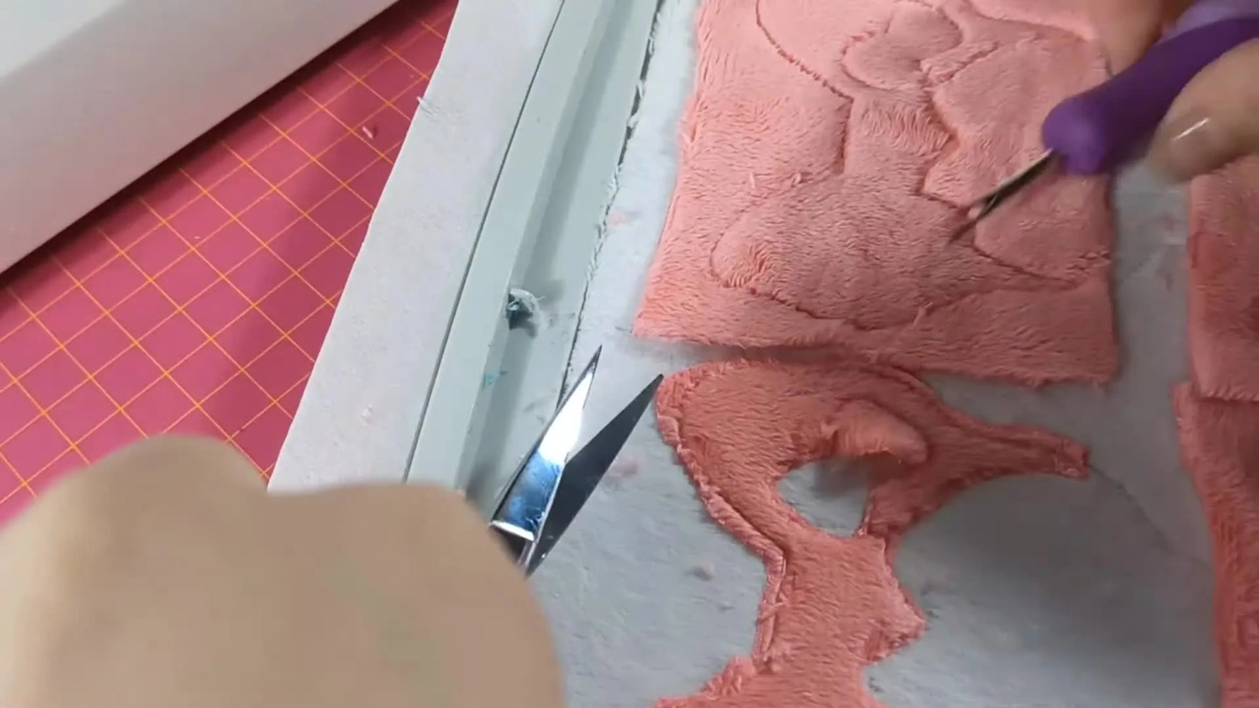 Close-up of the seam ripper lifting minky while curved scissors cut a clean window opening inside the bow appliqué area.