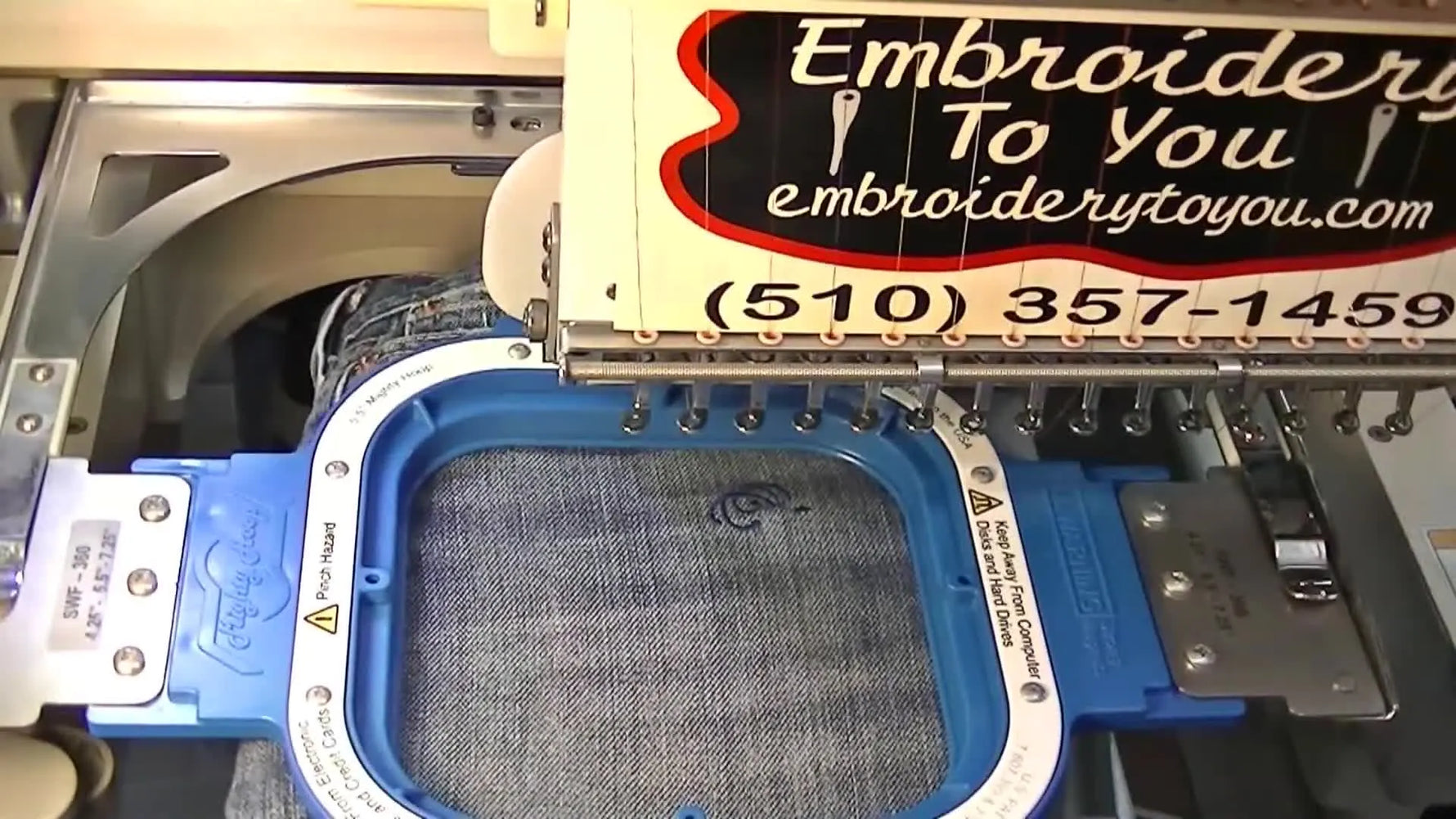 Wide view of women’s jeans loaded on the tubular arm of an SWF embroidery machine with a magnetic hoop clamped in place for pocket-area stitching.