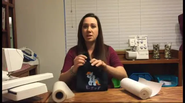 The instructor holds a black knit T-shirt while explaining how to stabilize knits so they don’t stretch during hooping.