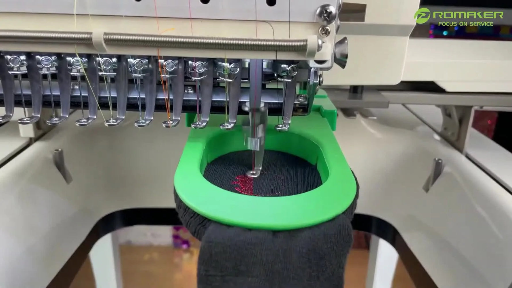A close-up of a multi-needle embroidery machine stitching a sock held in a narrow green clamp frame.