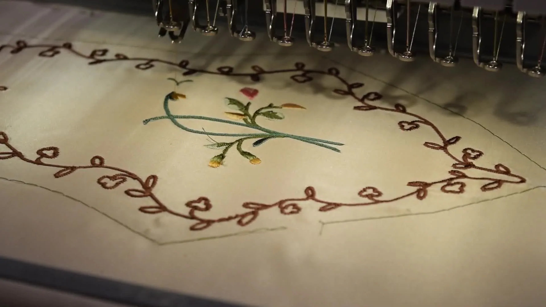 A close-up of a floral embroidery design stitching cleanly on silk with the texture clearly visible under bright light.