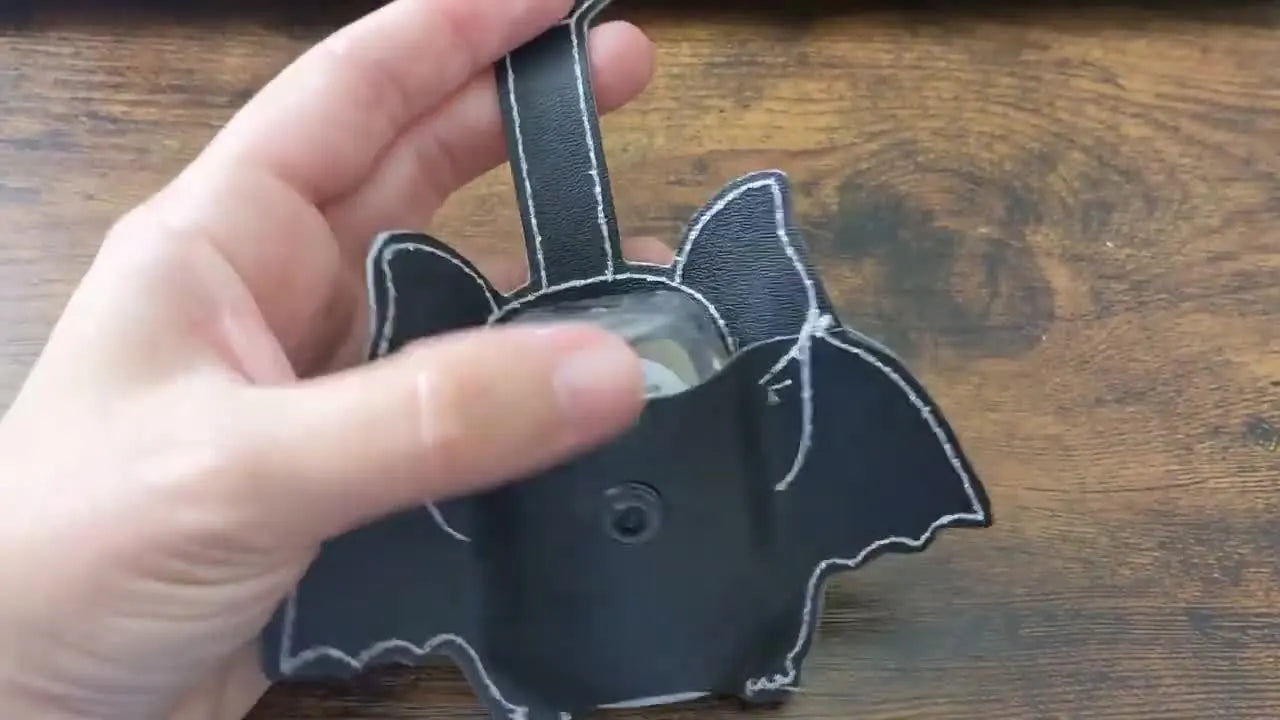 A finished bat-shaped in-the-hoop sanitizer case is shown with a bottle inserted, demonstrating the pocket fit and final shape.