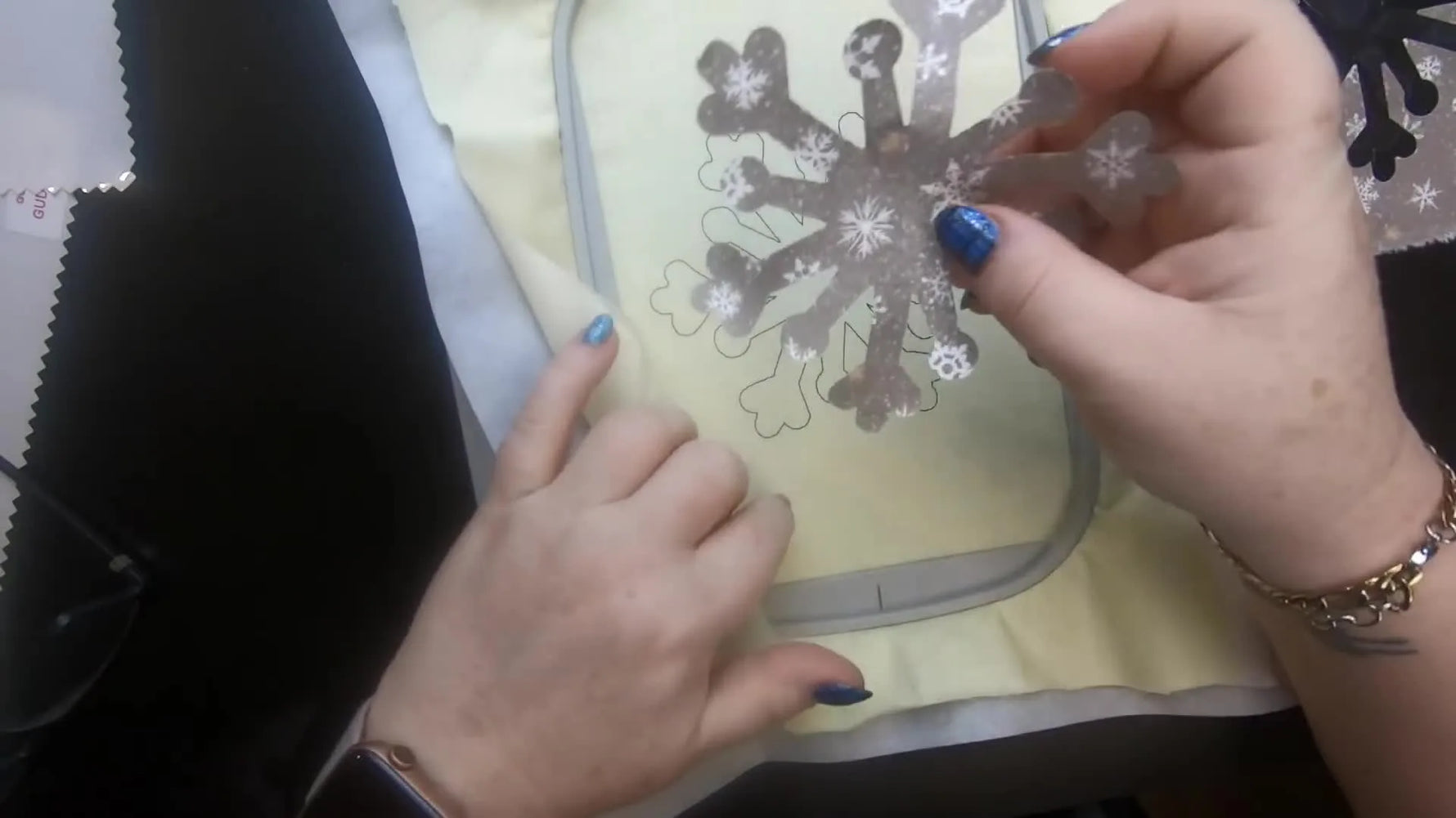Hands align a sticky snowflake appliqué precisely inside a stitched placement line in a hooped fabric.