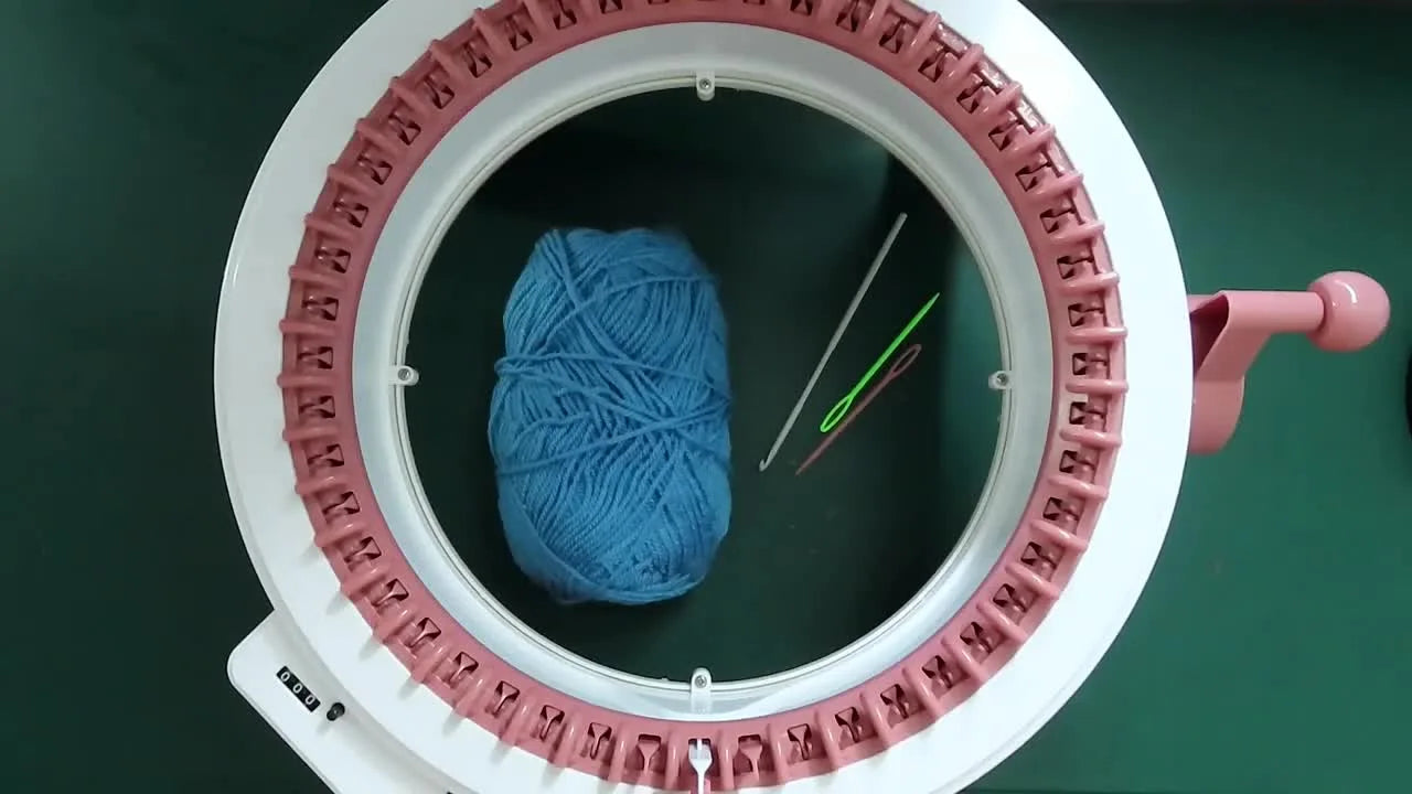 Sentro knitting machine with blue yarn, crochet hook, and bodkin needles.