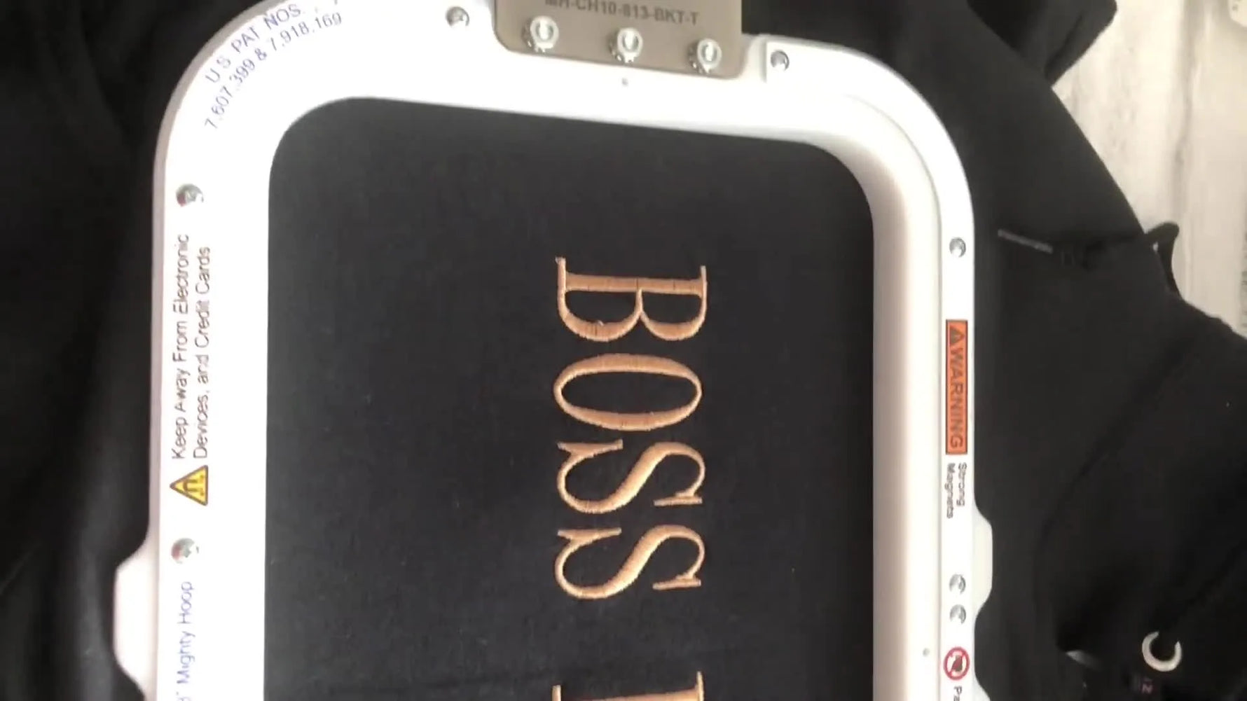 The finished “BOSS LADY” gold embroidery is shown clean and legible on a black hoodie while still held firmly in the 8x13 magnetic hoop.
