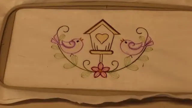 A finished birdhouse embroidery sits perfectly aligned inside a 5x12 multi-position hoop, showing a clean join between the top and bottom stitch-outs.