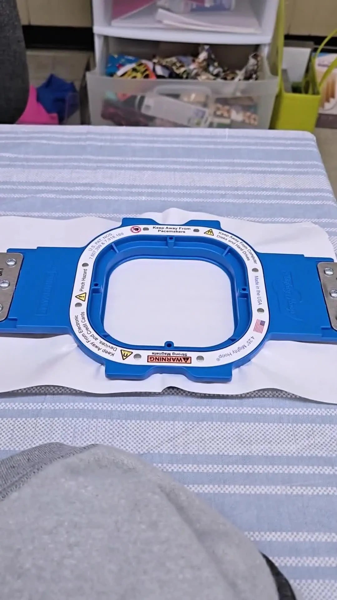 A blue magnetic hoop holds a sheet of white stabilizer on a worktable, ready for the sticky “float” method.
