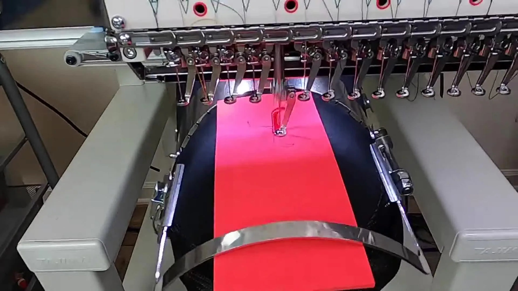 A close-up action shot of a Tajima head stitching a red satin letter over 3D foam on a cap, showing the presser foot gliding smoothly.