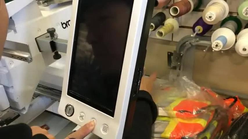A close-up of the Brother PR1000e control panel as a finger holds the Automatic Needle Threader button while powering on to enter Software Update Mode.