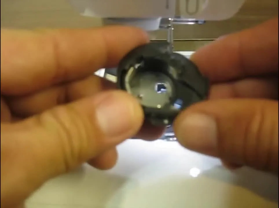 A close-up of the Brother SE400 bobbin case alignment mark (white arrow) that must match the white dot on the metal race during reassembly.