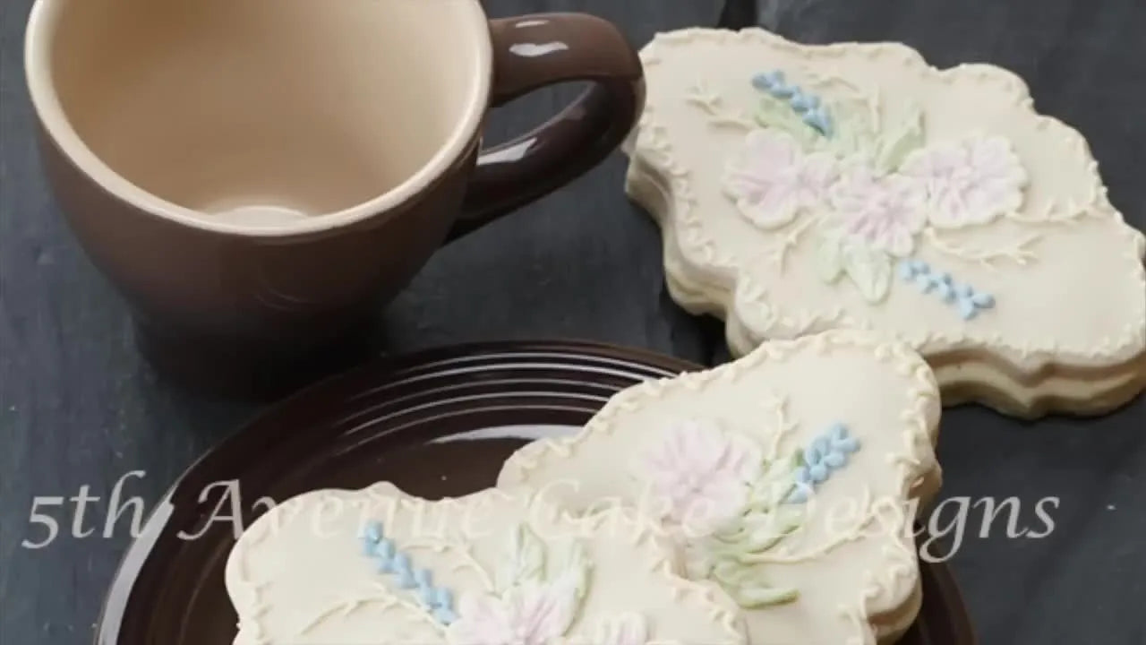 Finished brush embroidered cookies on a plate next to a mug.