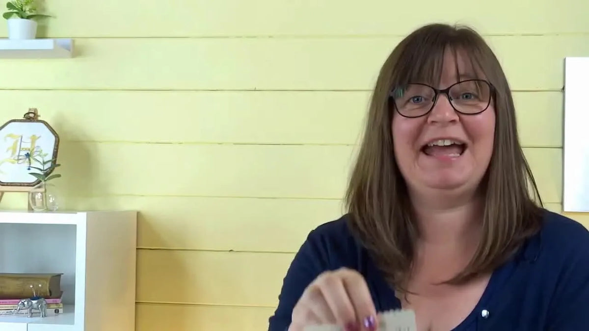 Presenter holding up a small cardboard packet of embroidery needles to the camera.