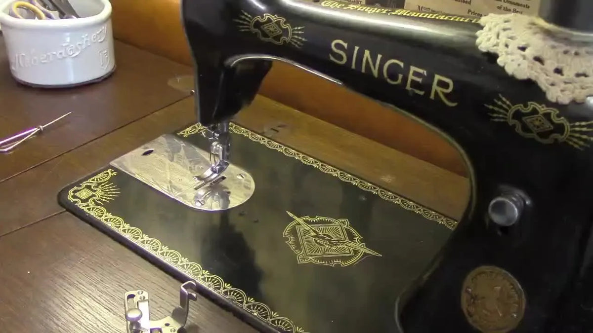 Vintage Singer sewing machine with various metal attachments laid out on a wooden table.