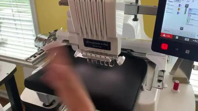 A close-up of the Brother PR670E stitching gold details onto a black neoprene laptop case while the bulky item is supported and kept clear of the needle path.