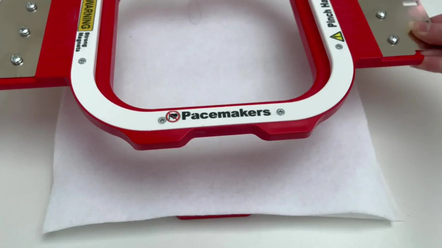 Hands snap a red magnetic hoop down over white felt and stabilizer, creating a clean, taut setup ready for a trace and stitch-out.