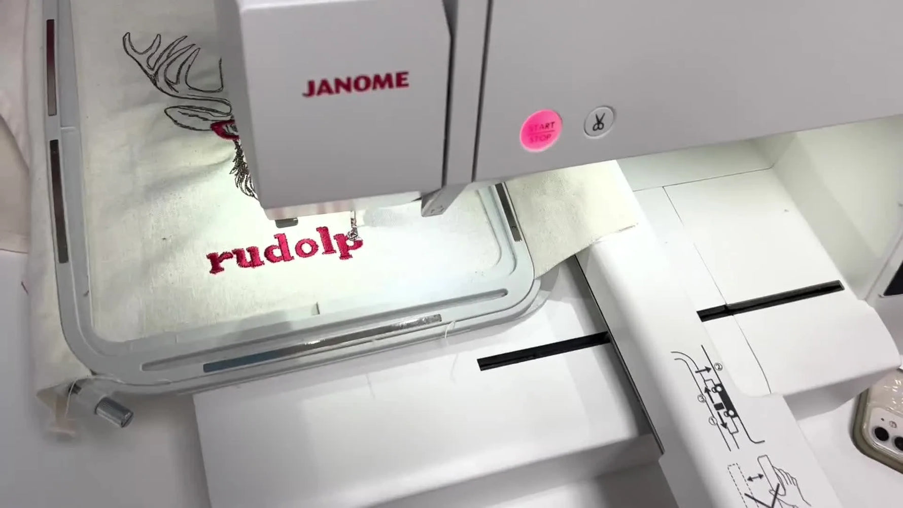 Close-up action shot of the Janome 500E stitching red name text while the hoop holds the tea towel steady.