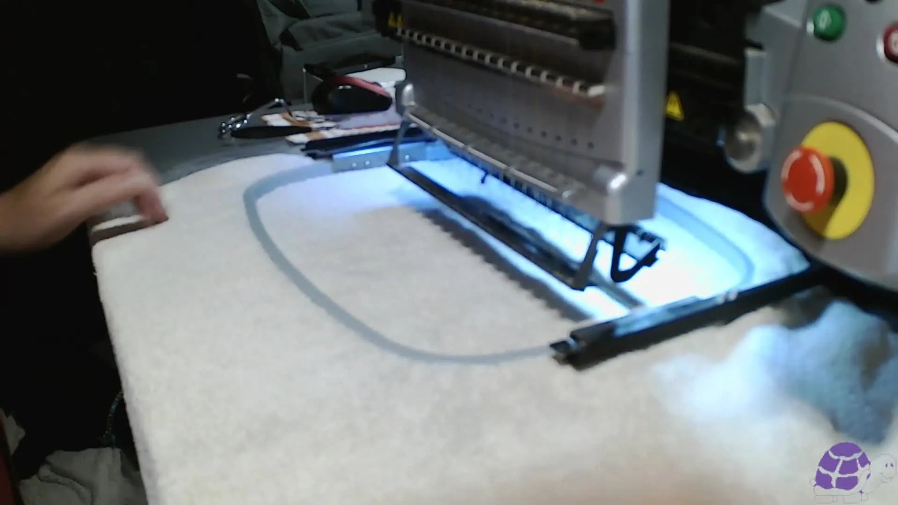 A close-up of the embroidery machine stitching the primer layer onto a towel through water-soluble topping.