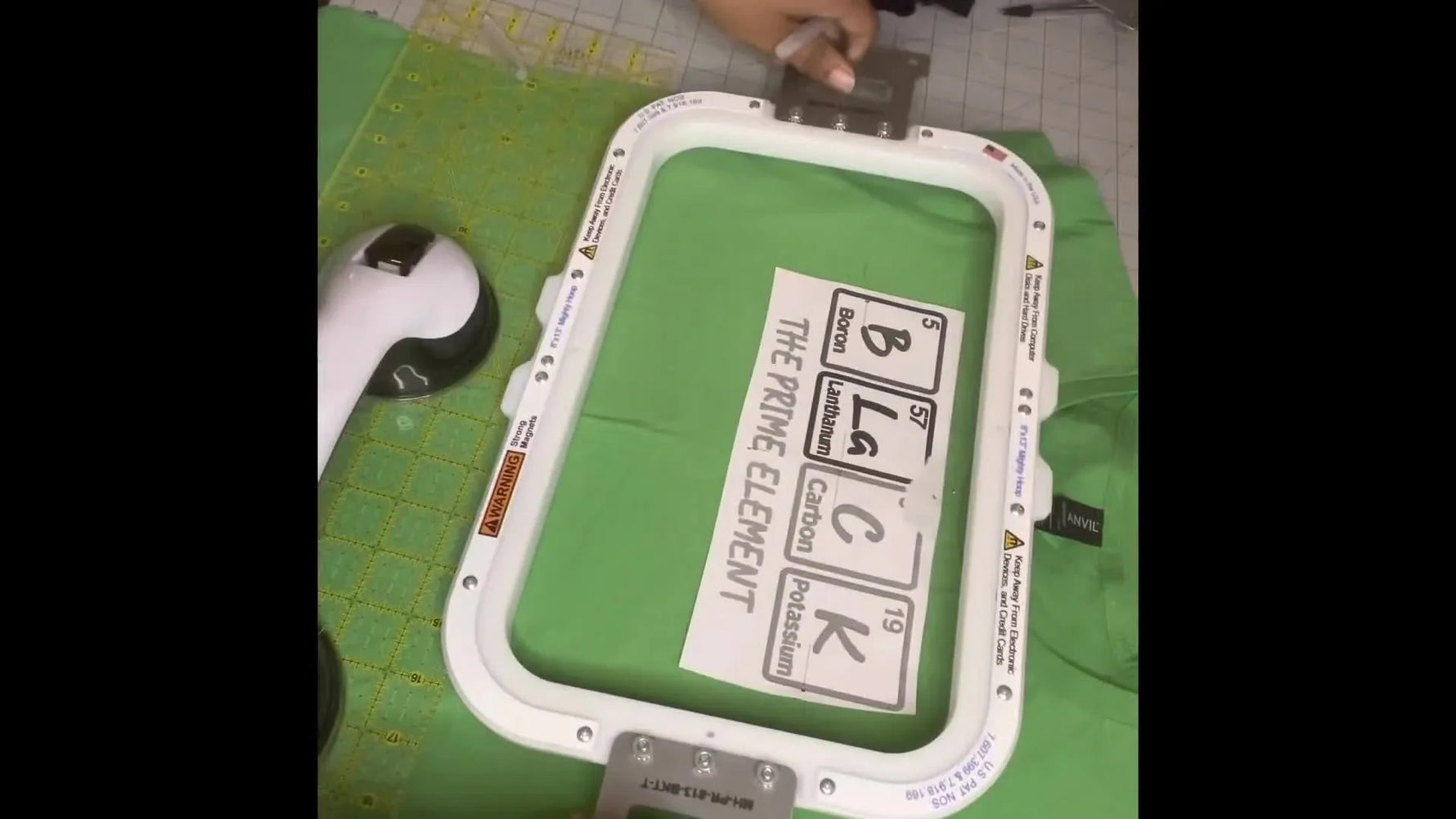 A rectangular magnetic embroidery hoop aligned to long crosshair markings on a green T‑shirt for perfectly centered chest placement.