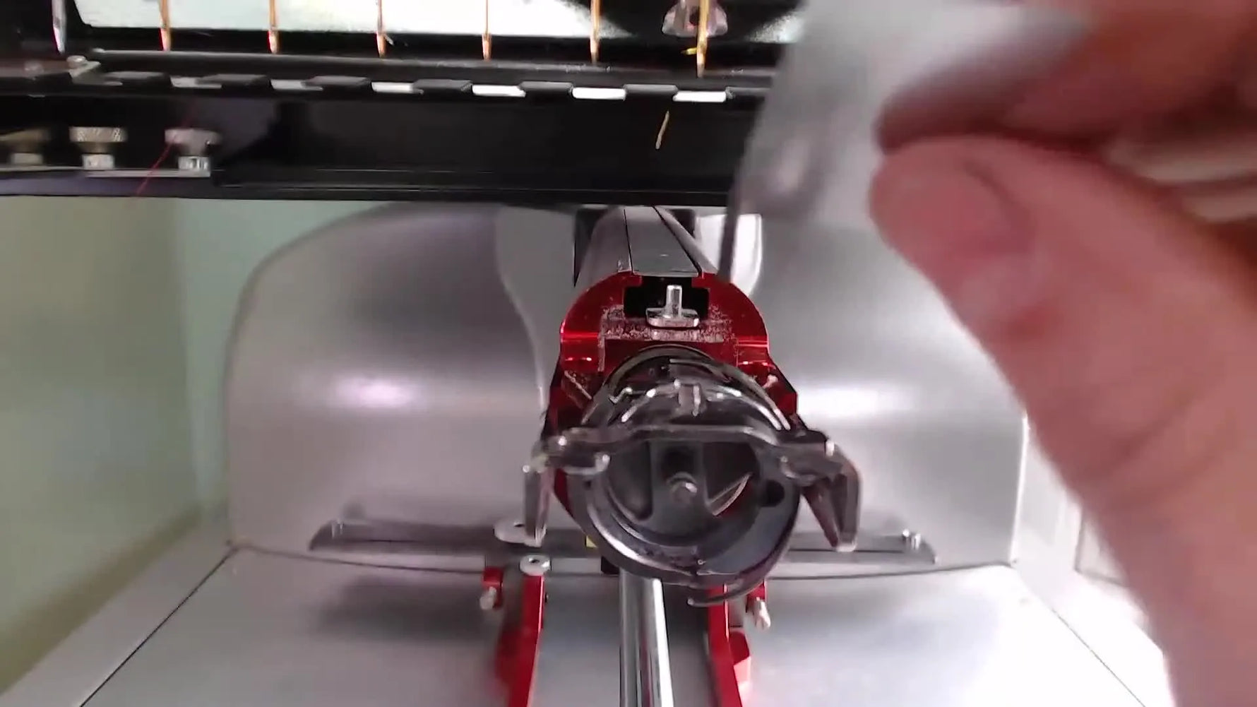 A close-up shows the metal finger gap tool inserted between the retaining finger and the rotary hook basket on a Melco EMT16X.