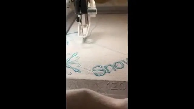 A macro close-up shows the needle tip dropping precisely into the corner of a green L-shaped registration mark for perfect multi-hoop alignment.