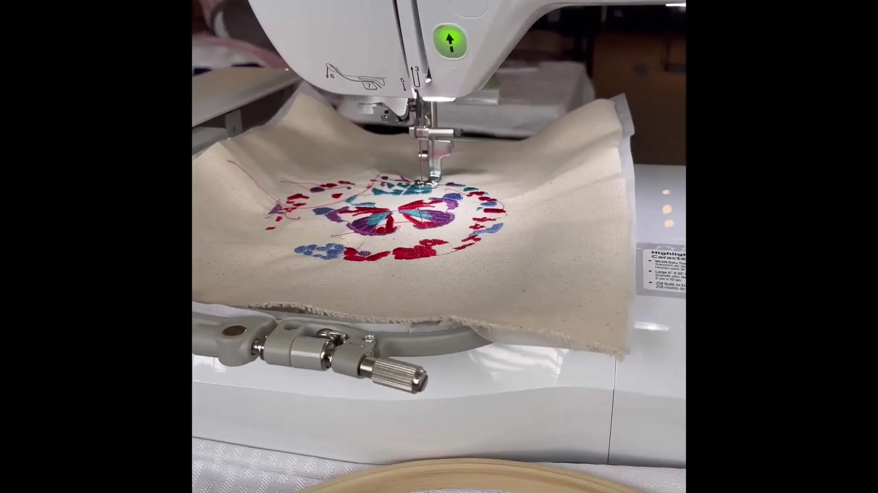 A Brother NQ1700E stitching a stained-glass butterfly design in the hoop, with the needle area and hoop clearly visible.