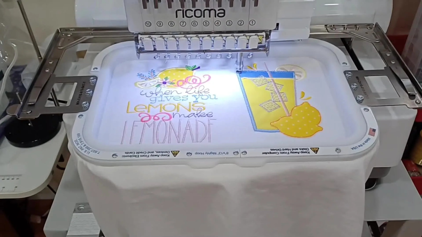 A finished white V-neck T-shirt is folded on a cutting mat, showing the completed lemonade-themed appliqué embroidery.