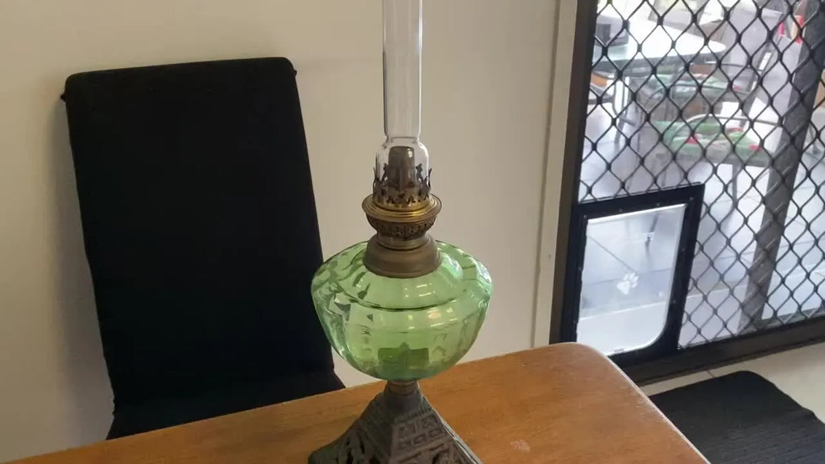 A vintage green glass oil lamp with a brass Cosmos burner and clear glass chimney.