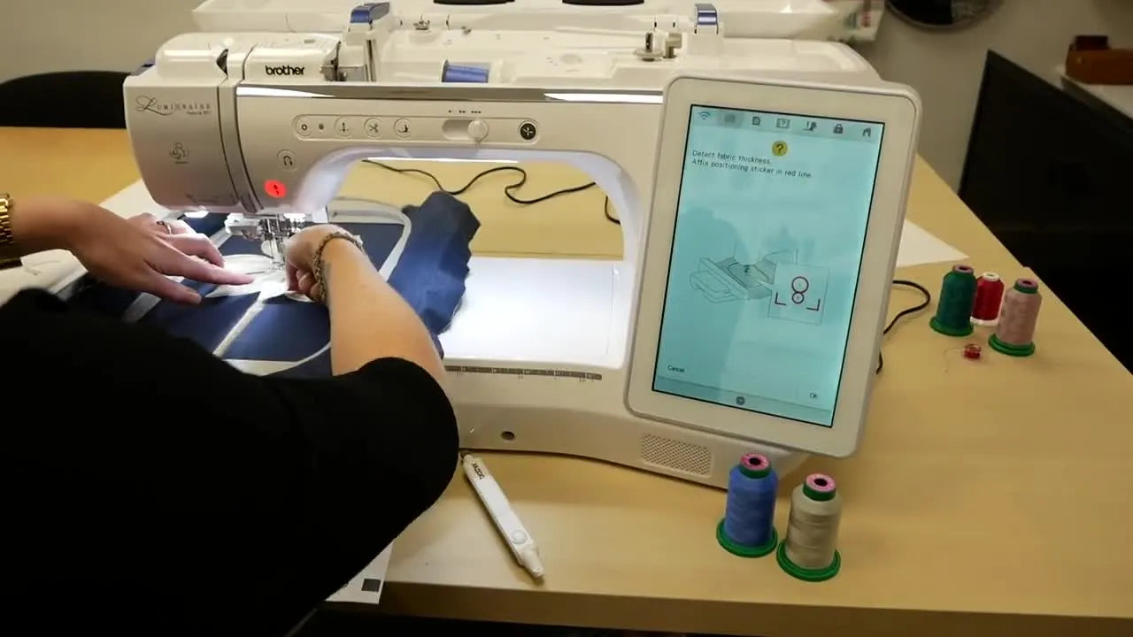 A Snowman positioning sticker is placed on hooped floral fabric to help the Brother Luminaire XP1 camera detect thickness before scanning.