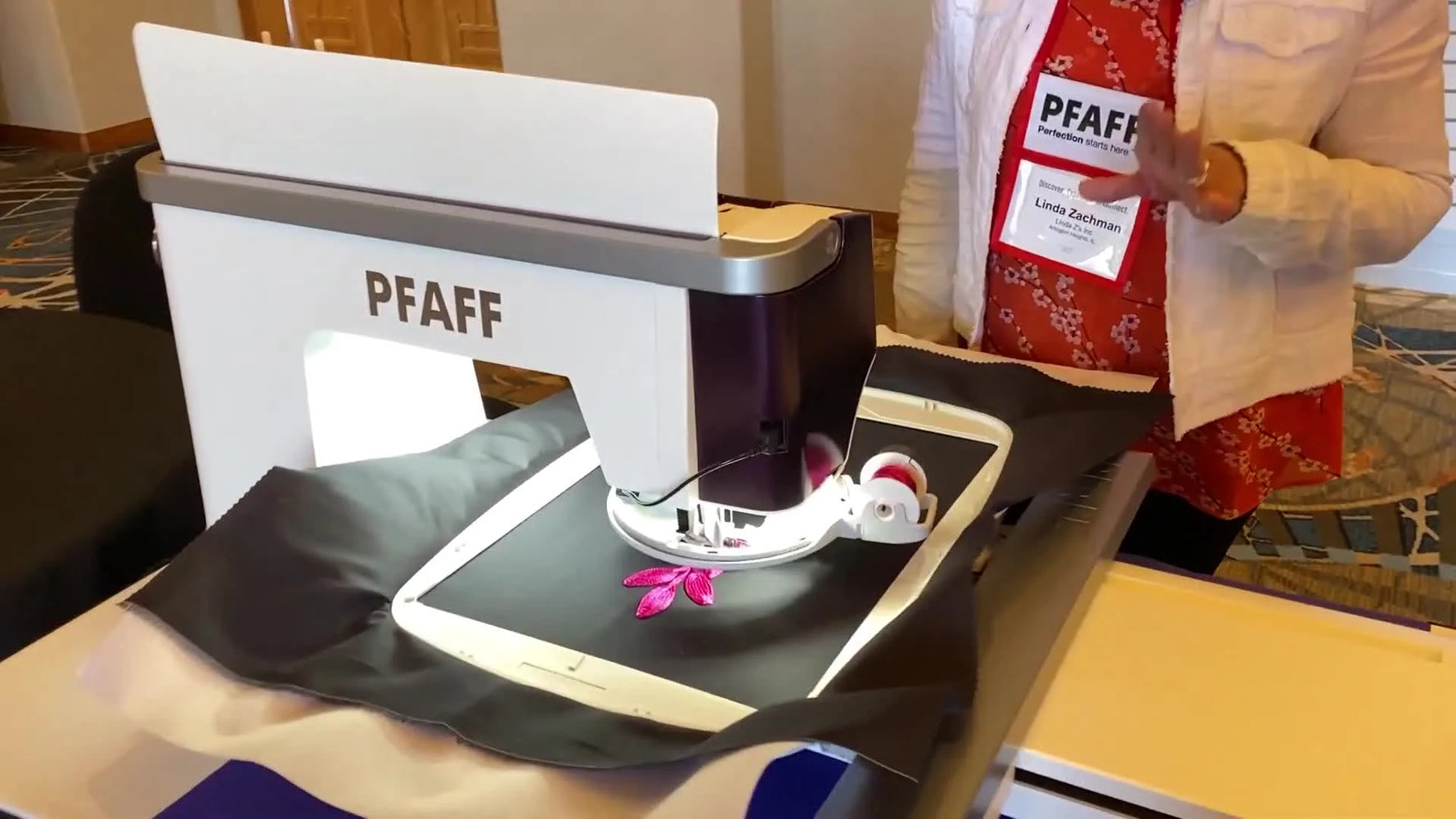 A close-up shows the Pfaff Creative Embellishment Attachment rotating as it feeds pink cording under the needle on black fabric.