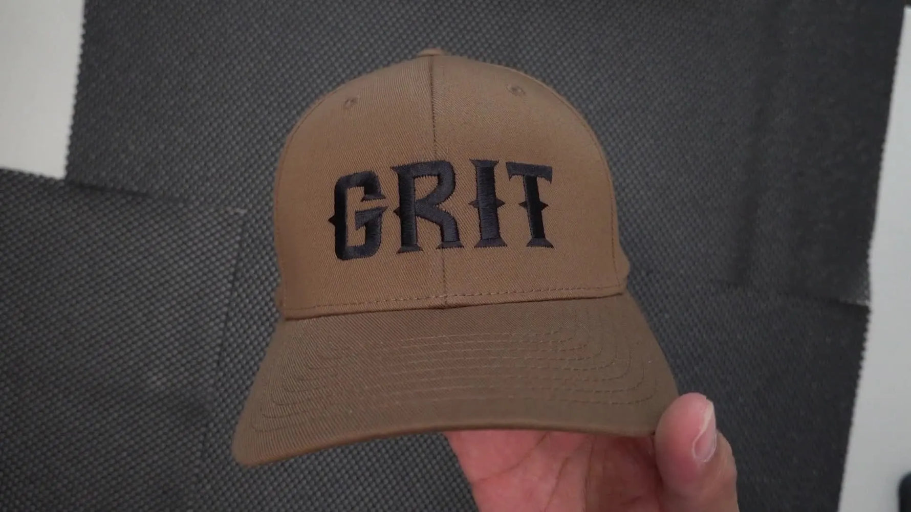 Close-up of a brown structured cap showing a bold black 3D puff-style satin stitch “GRIT” embroidery result.