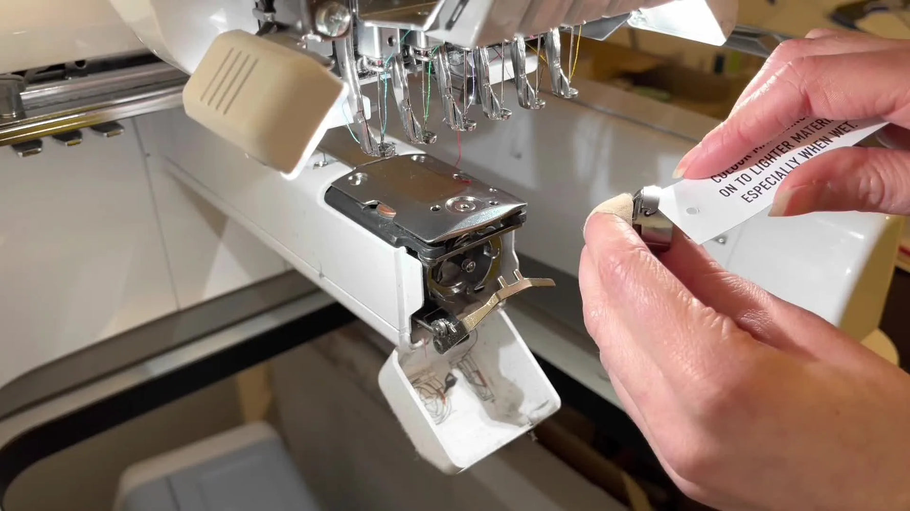 An extreme close-up shows a thin card sliding under the bobbin case tension spring to clear hidden lint that can mimic tension problems.