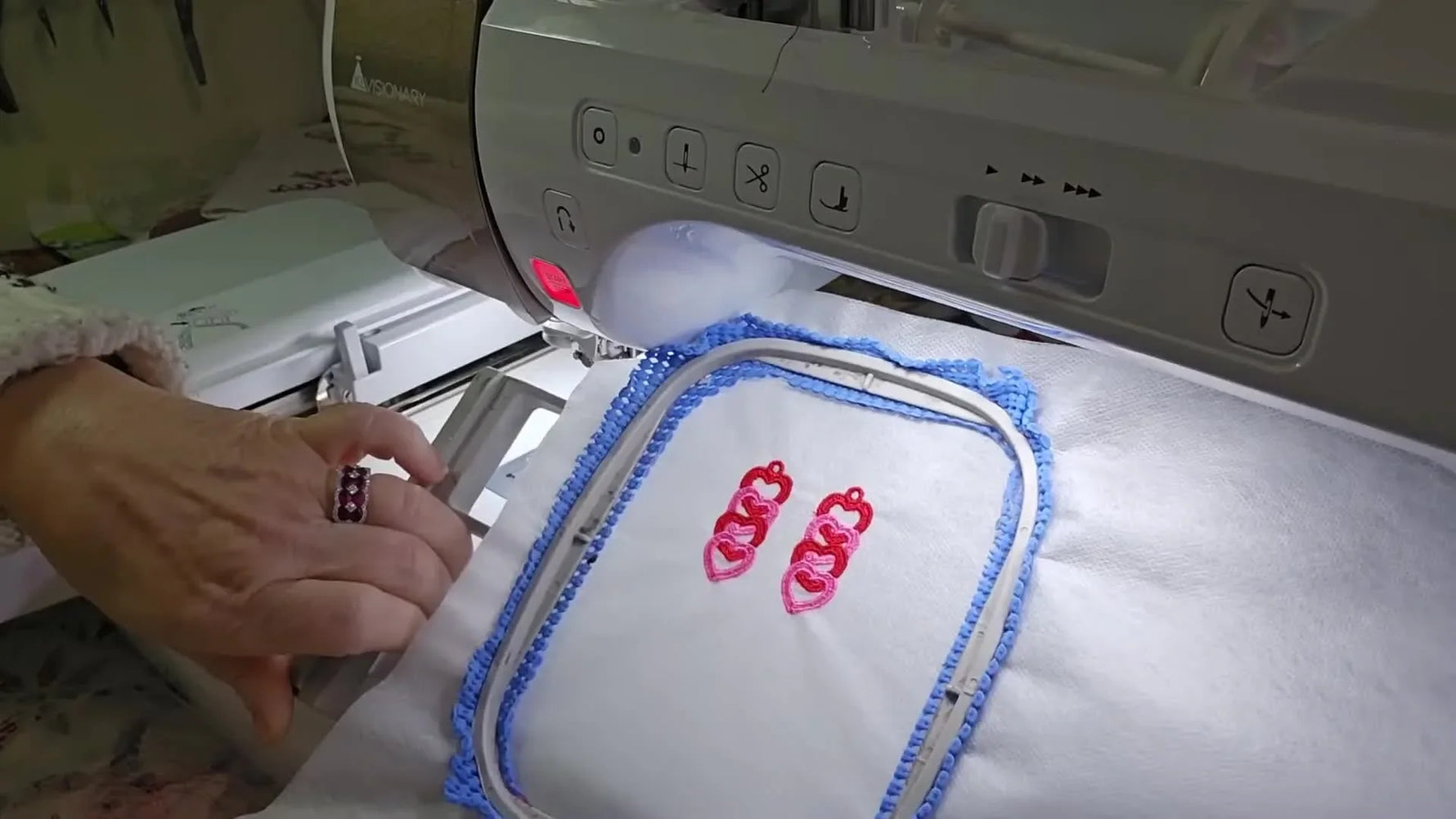 Completed freestanding lace interlocking heart earrings shown in the hoop with red and bright pink stitching still supported by water-soluble stabilizer.