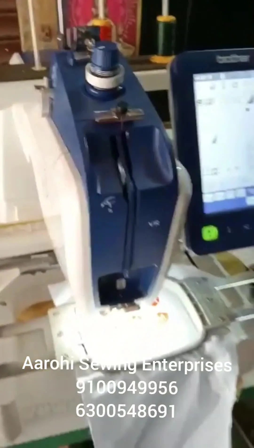 A close-up of a Brother VR single-needle machine stitching red shield logos in a small tubular hoop on white fabric.