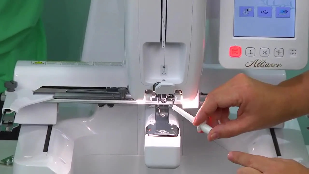 Using a white forked tool to place the blue thread into a guide above the needle.