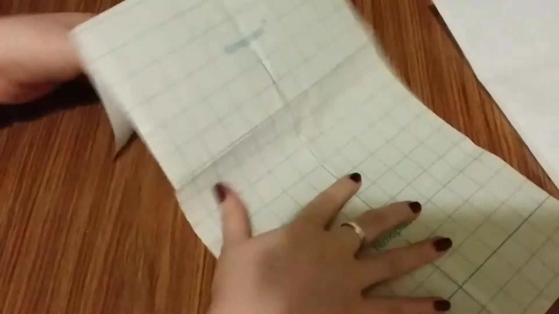 An overhead view of a Filmoplast-style sticky-back stabilizer sheet with a green grid backing being unfolded on a wooden table.