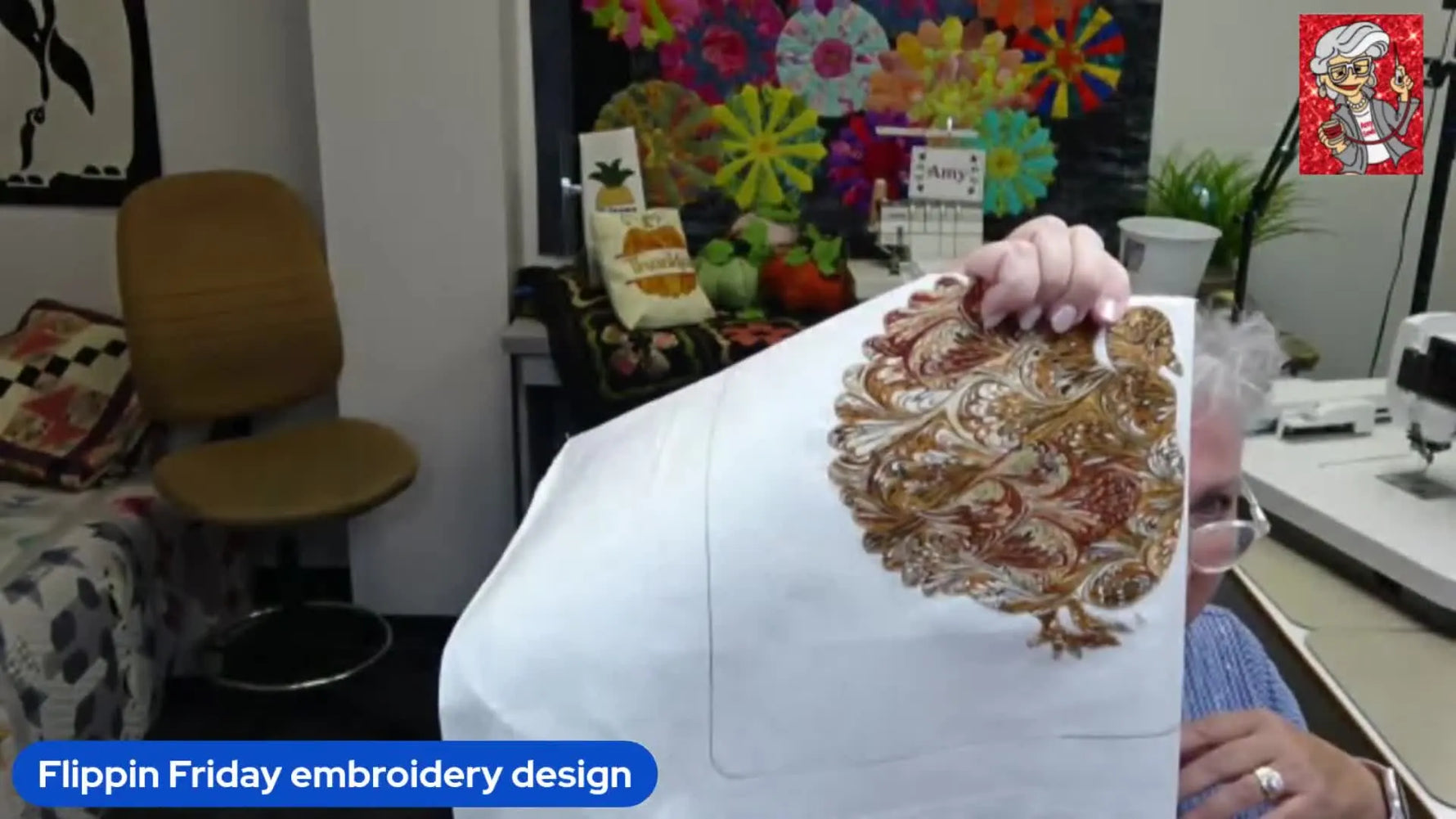 Hands holding up a white fabric with an embroidered turkey design in shades of brown and gold.