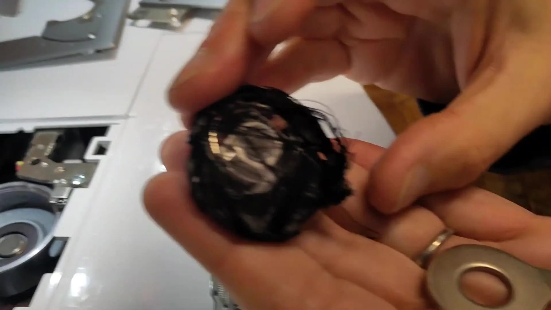 A close-up of the bobbin case wrapped in a massive black thread bird’s nest, showing the exact kind of jam that can lock a Brother Innov-is hoop in place.