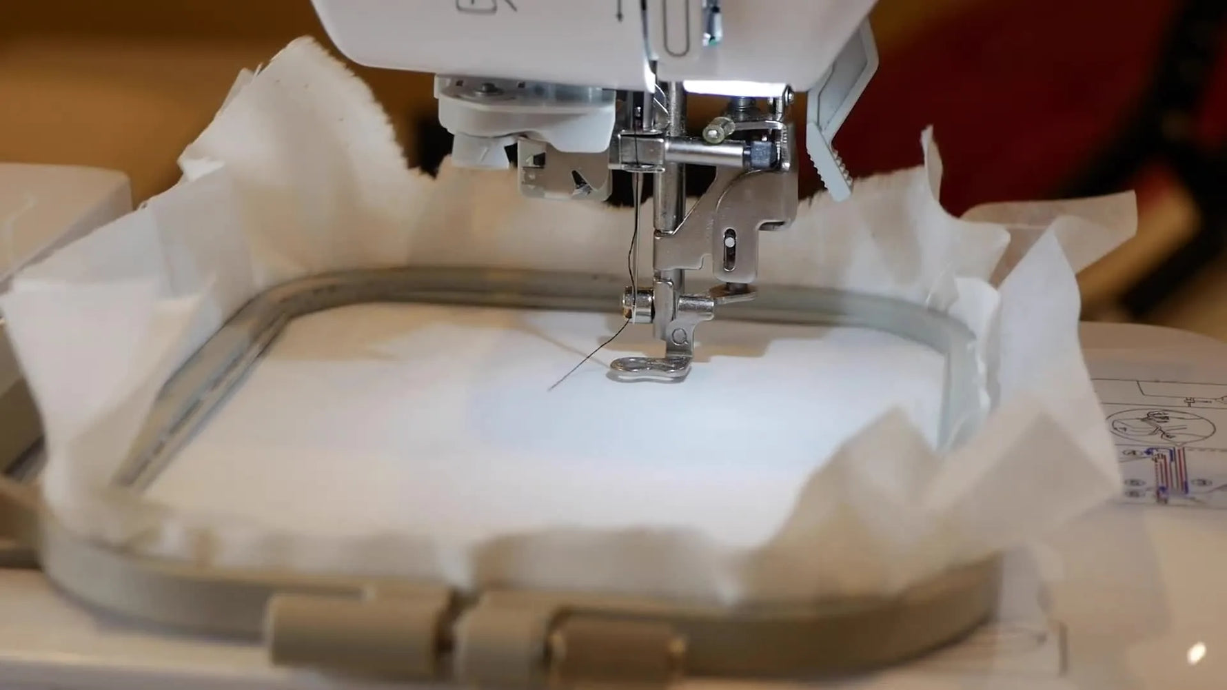 A close-up of the Brother SE600 actively stitching black thread onto white fabric during the “Slam Can” design run.