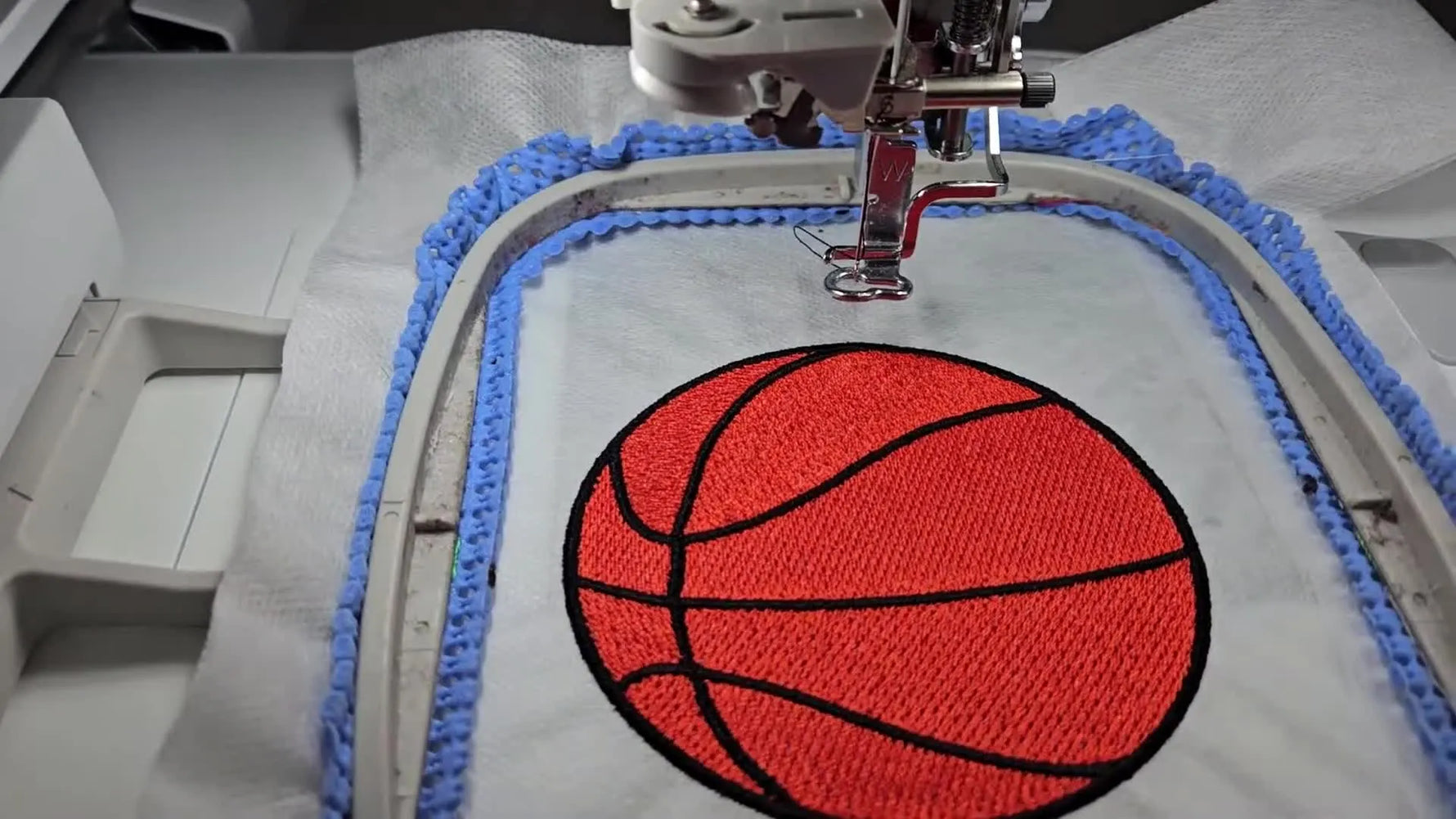 A finished freestanding lace basketball design sits perfectly centered in the hoop, showing crisp orange fill, black seam lines, and a dense satin border.