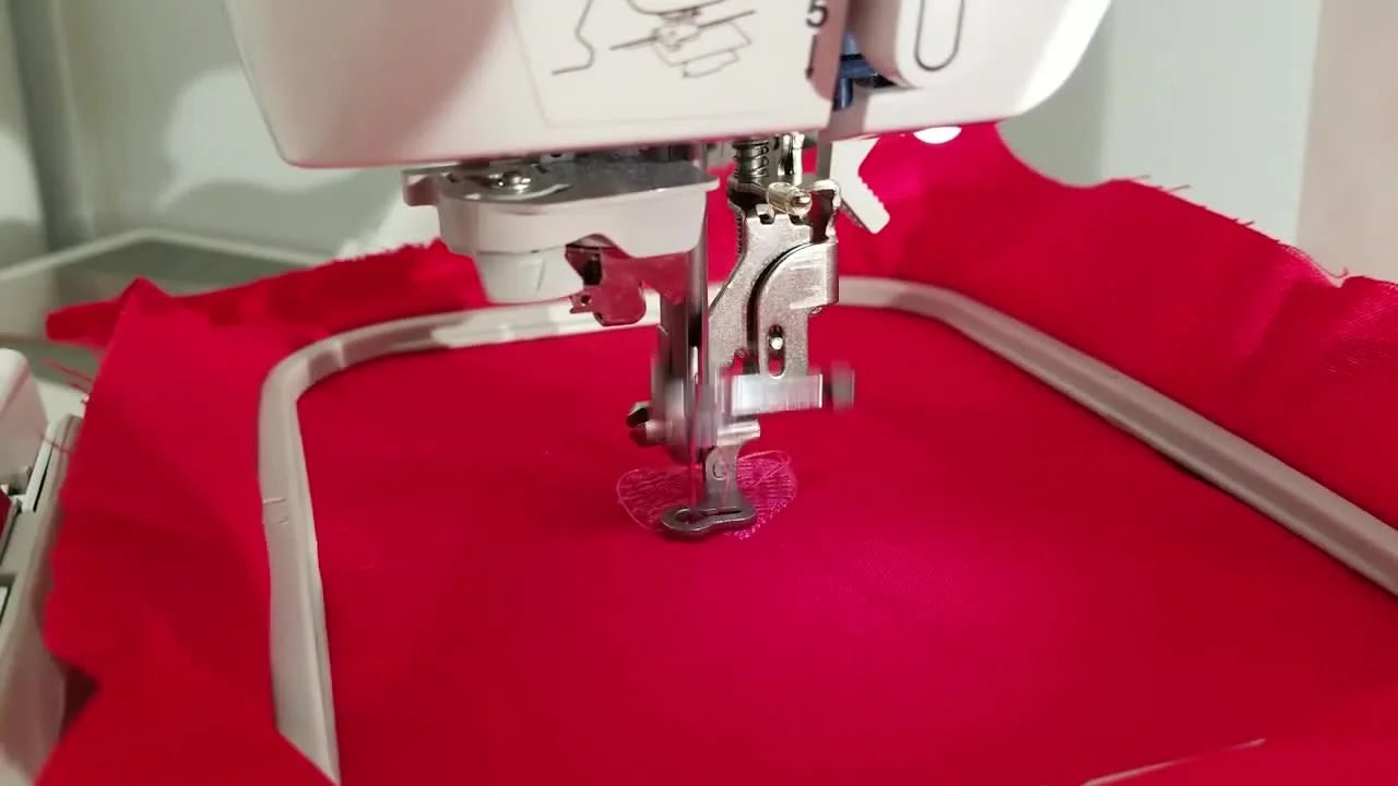 A close-up of the Brother SE 425 stitching a satin border around a pink heart on red fabric.