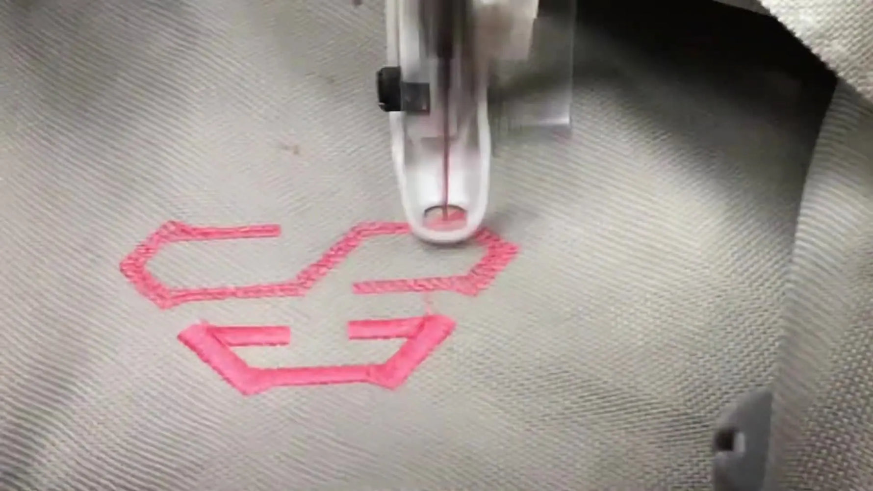A Husqvarna Viking embroidery machine stitches the center letter of a pink satin monogram while magnetic holders clamp the canvas flat in a metal hoop.